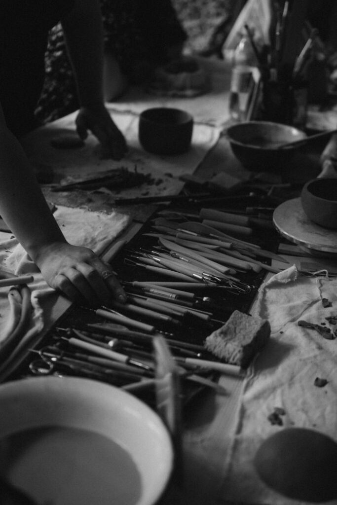 Black and white close-up of hands arranging tools in a creative workshop setting.
